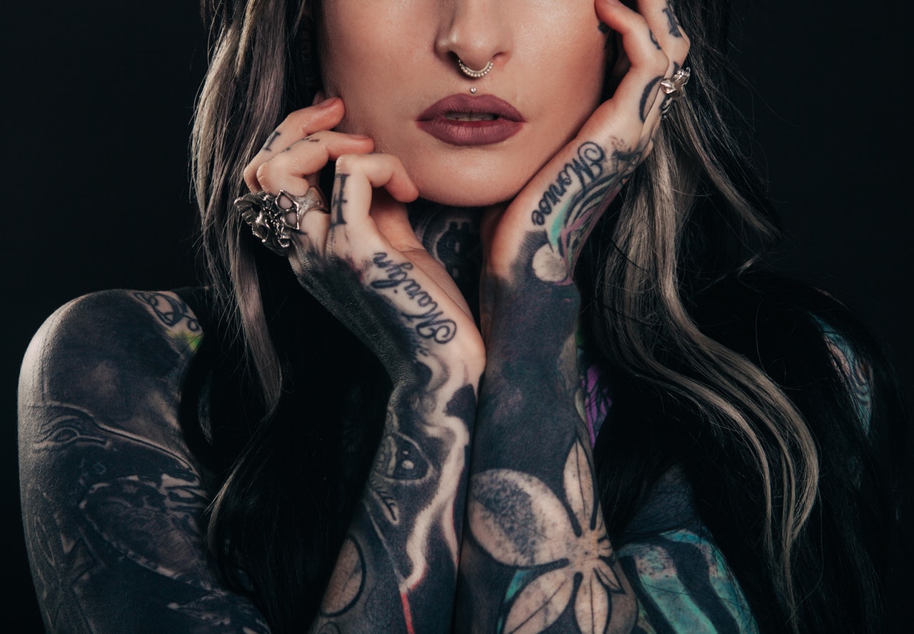 A woman with a nose piercing and tattoos on her arms, hands and neck